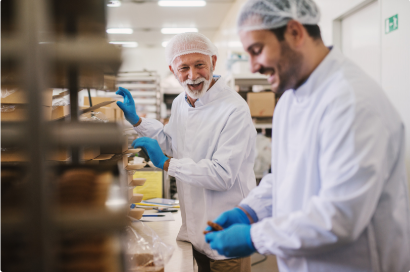 two male food factory employees in sterile clothes packing fresh made cookies