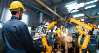 man with programming laptop monitoring robotic arm 